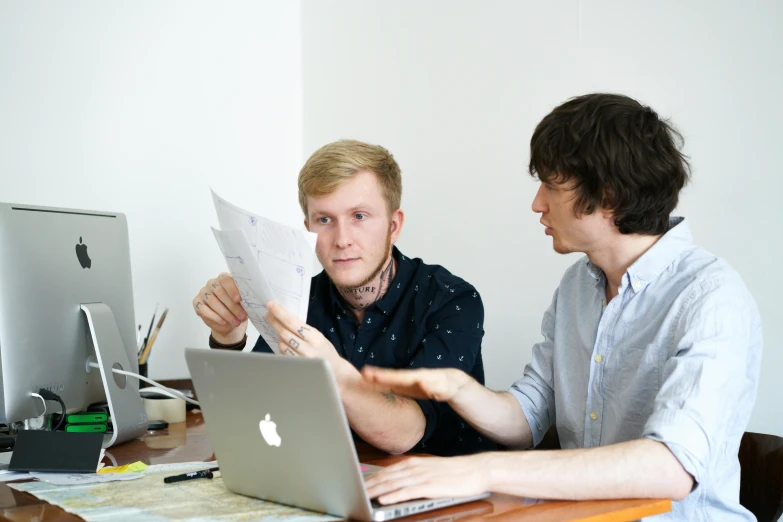 two men looking at paper near laptop on desk