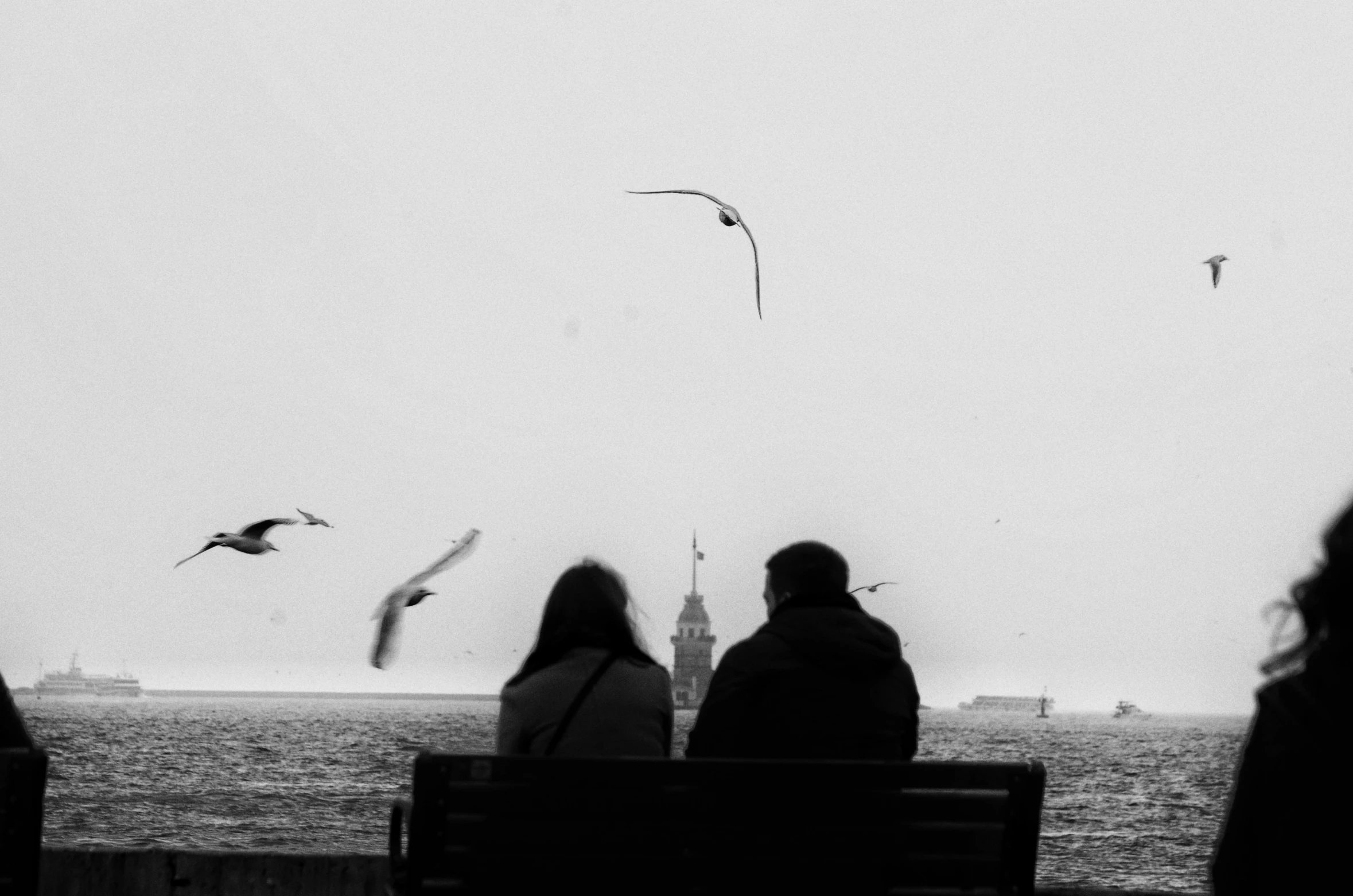 a black and white po with people sitting on a bench in front of the ocean