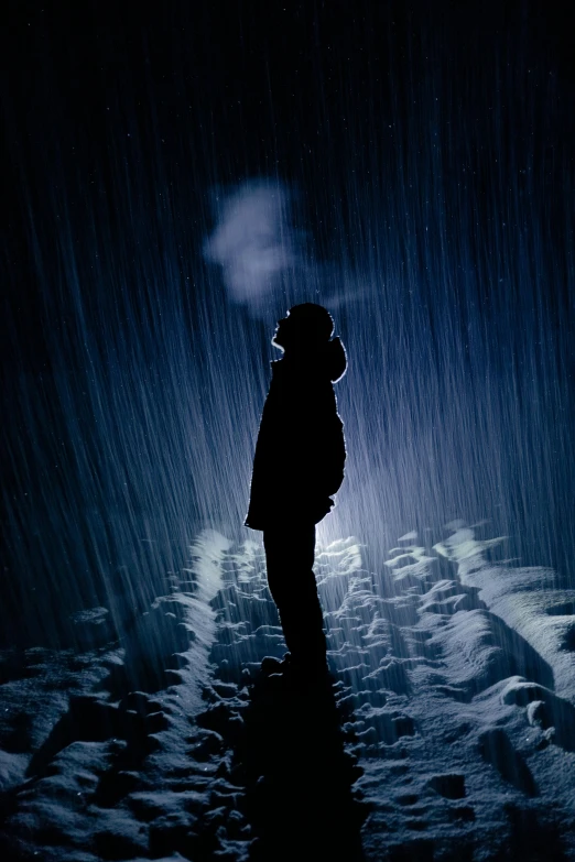a person standing in the snow at night with their silhouette illuminated by the light of the bright umbrella