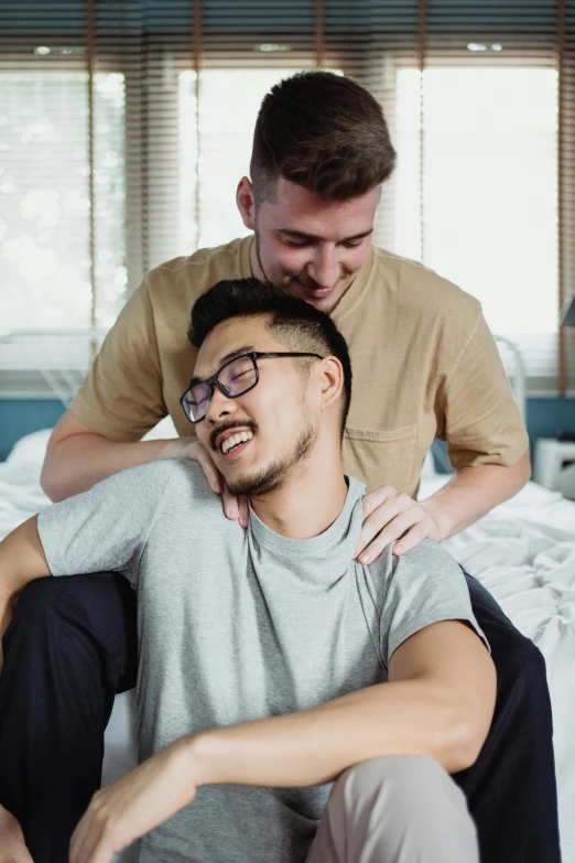 a man sits on a bed, with another man in his arms