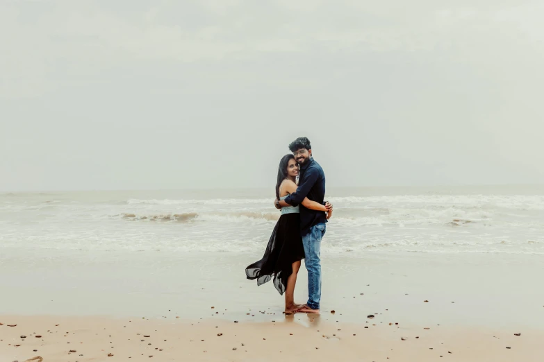 the couple is hugging on the beach by the ocean