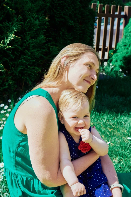 woman holding baby with both arms and sitting on grass