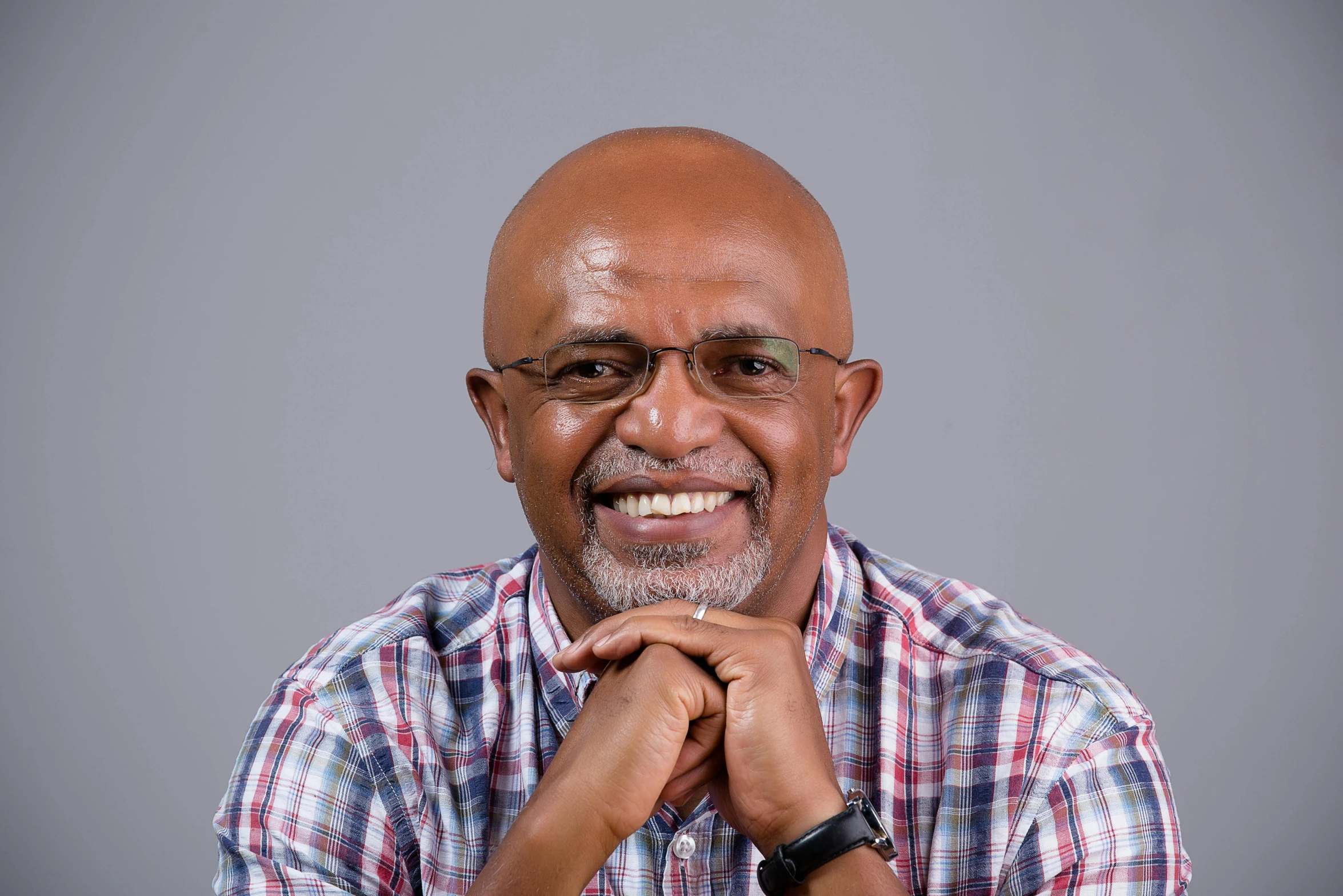 a smiling elderly man with glasses and a checkered shirt