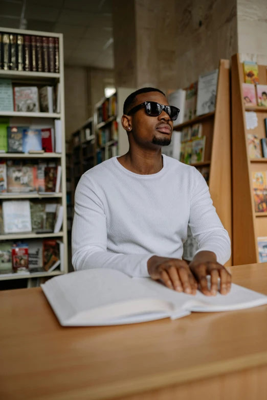 man in white shirt sitting at desk reading a book