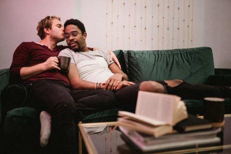 two young men are laying on a green couch