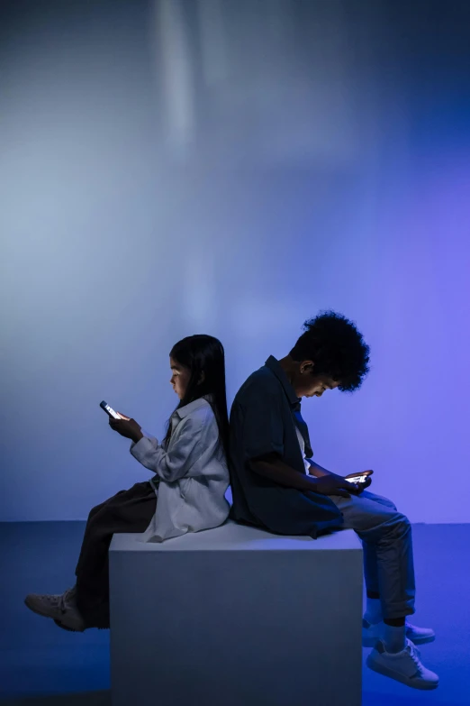 two people sitting together using cell phones in the dark