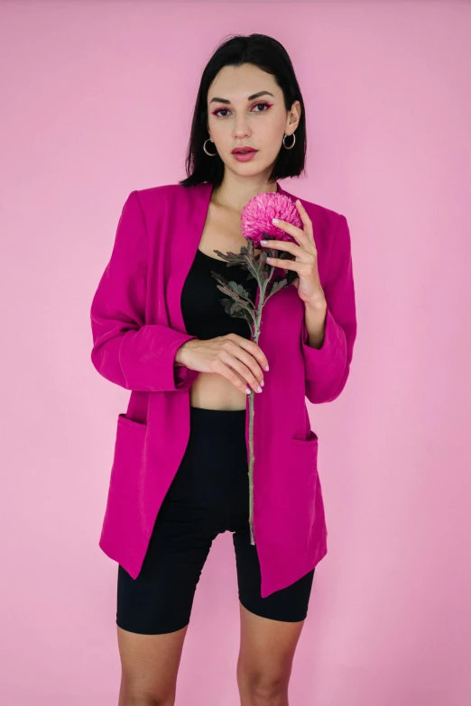 a woman holding a pink flower standing next to a pink wall