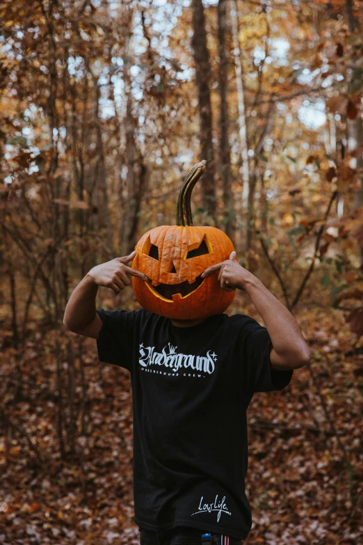 a  holds a jack - o'- lanterns head while looking out towards the woods