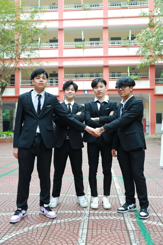 five boys wearing suits are shaking hands in front of a building