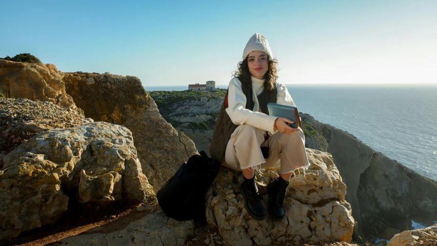 a young woman sits on a cliff overlooking the ocean