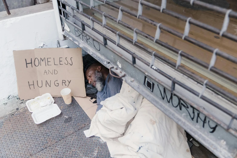 a homeless man looking out from the bottom of his bed