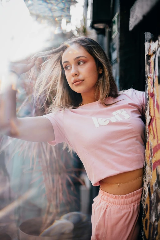 woman in pink top leaning up against wall with skateboard