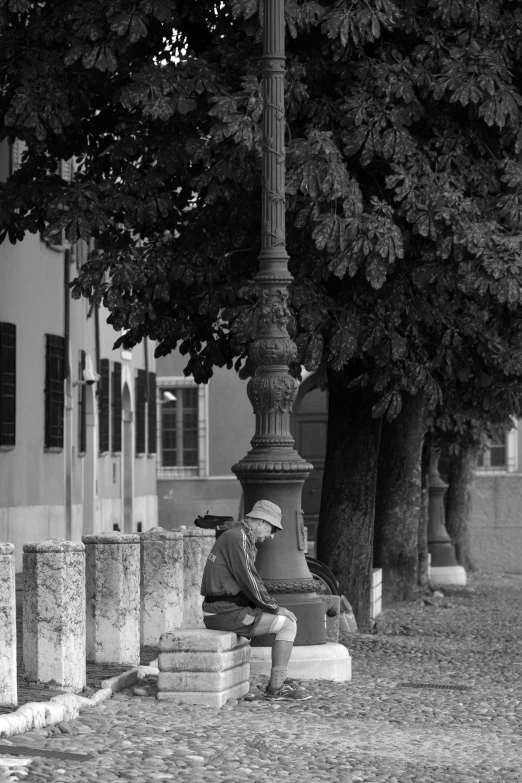 a person sitting on a street bench by a tree