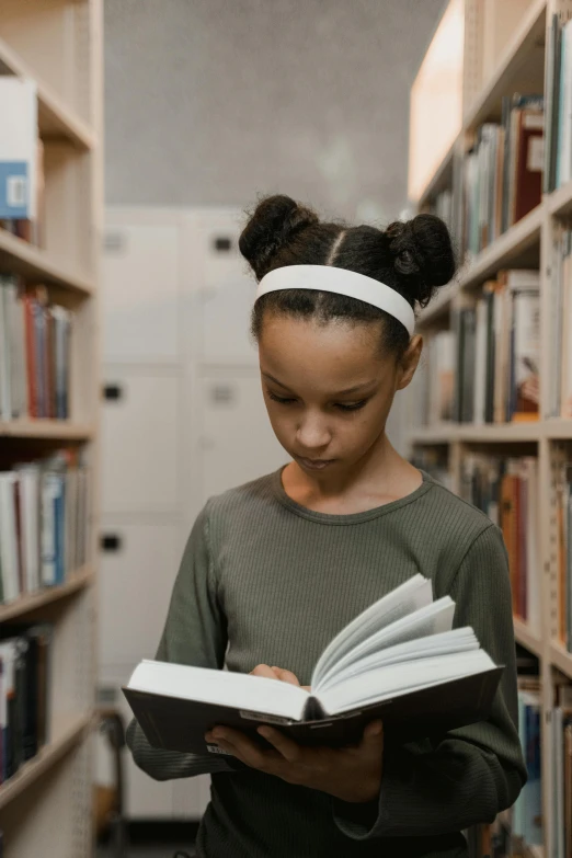 a little girl reading a book in front of a bookshelf