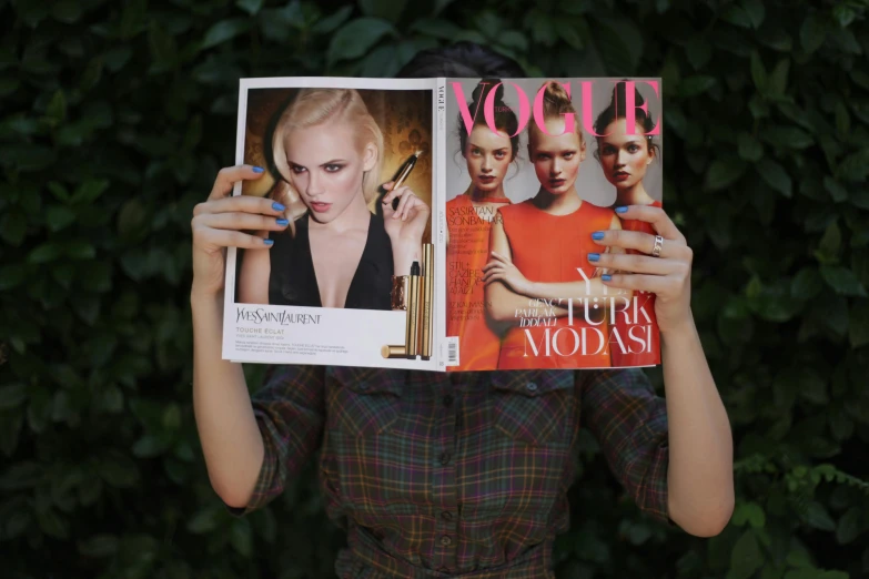 a woman holds up a magazine in front of her face