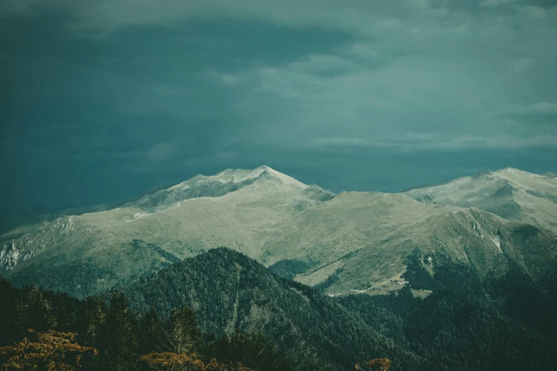 a group of mountain range during the day, with clouds hovering above them