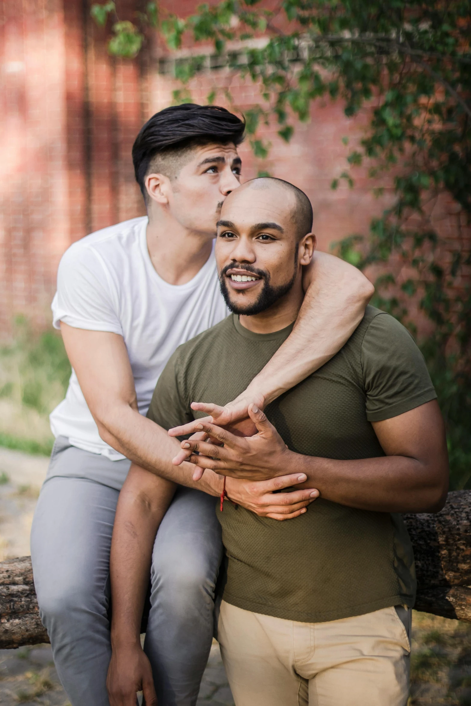 two men sitting on the log of a tree, one is being hugged by another man