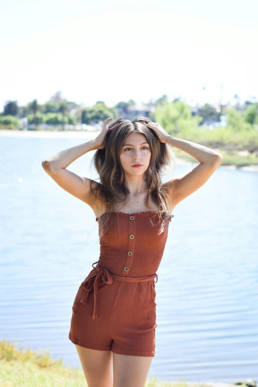 a woman standing near a lake is holding her hands on her head