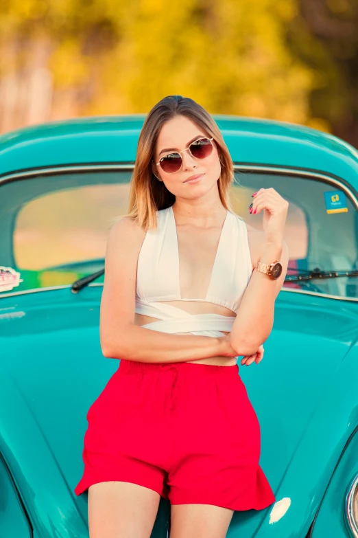 a woman in red shorts leaning on an old vw bug