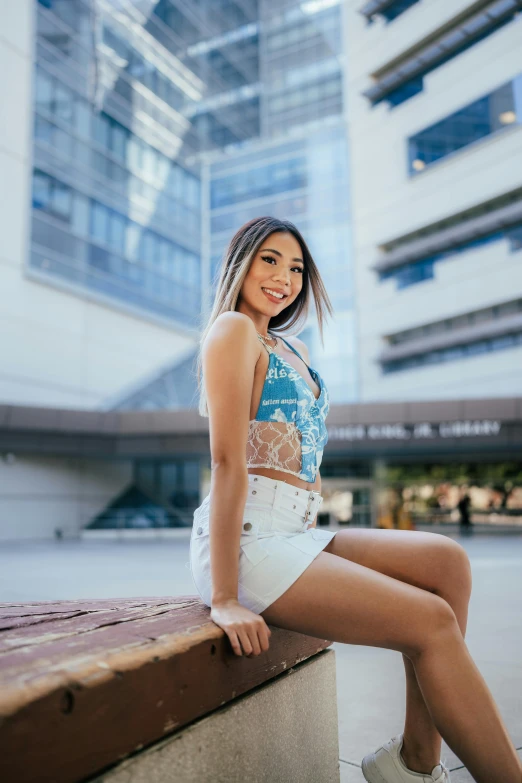 a beautiful young woman sitting on a ledge with high rise building in the background