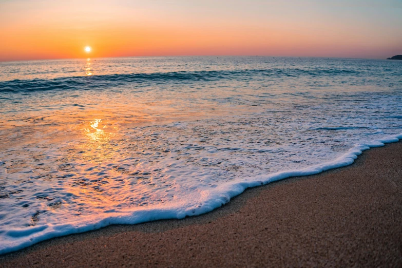 a sunset over the ocean with waves on the beach