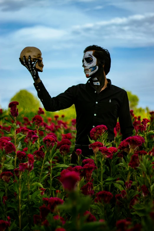 a man with paint on his face holding a skull in the middle of flowers