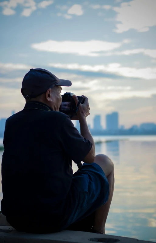 man sitting by the water taking pos with a camera