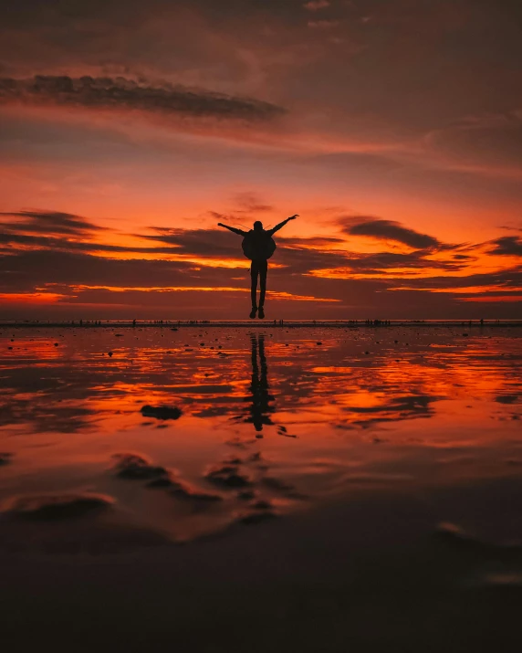 the silhouette of a person in a wetsuit stands at sunset