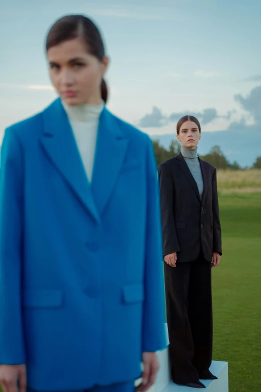 two women stand on pedestals in front of a field