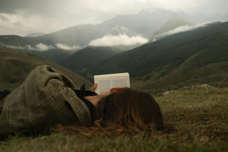 a person laying on top of a lush green hillside reading