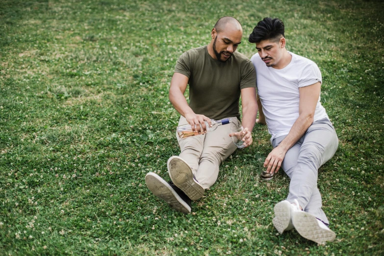 two men sitting on a grass field one is tying a shoelace