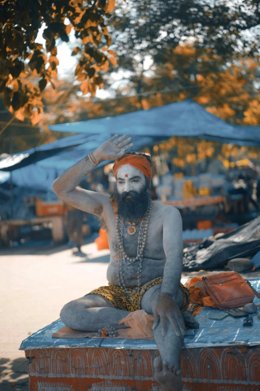 the man is sitting and wearing a turban and white painted face