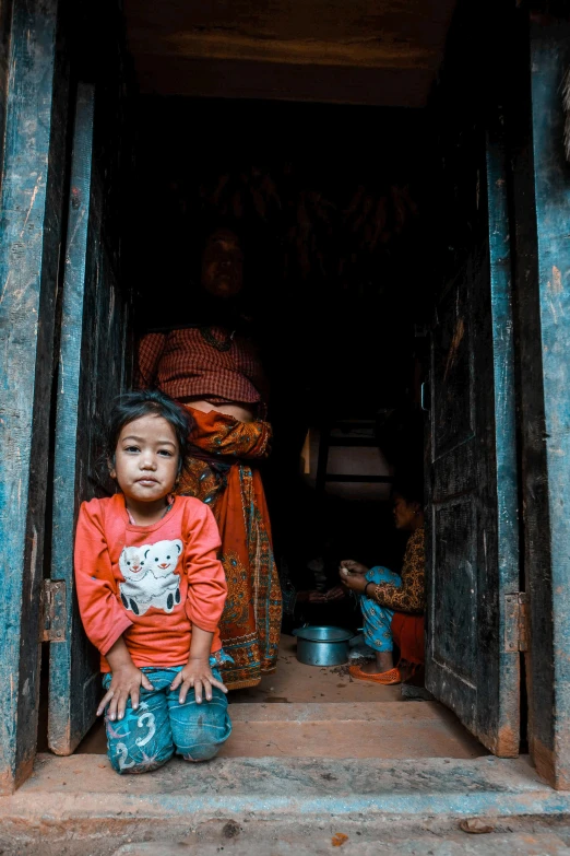 a little girl sitting in a doorway looking at the camera