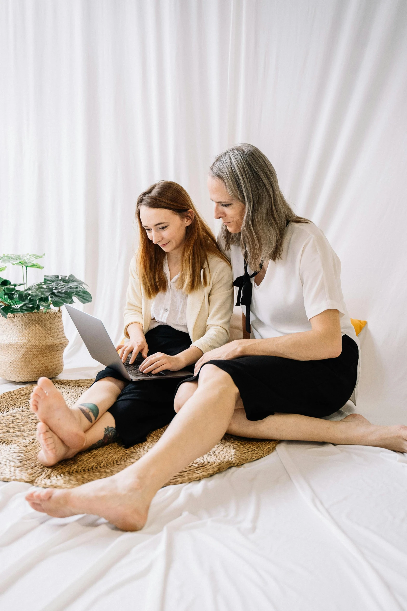 two people sit on the ground using their laptops