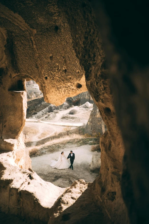 bride and groom standing inside of cave with valley in the background