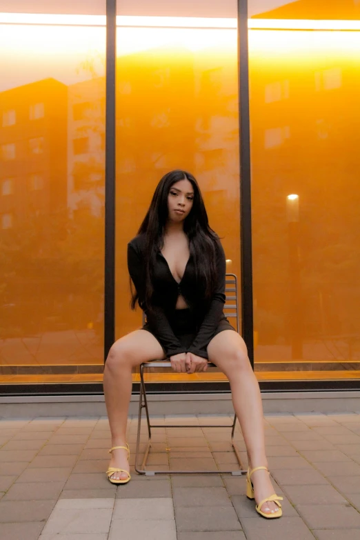 a woman with long black hair wearing heels and sitting on a chair