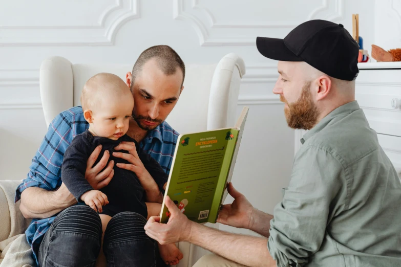 two men are sitting down and one of them is holding a book and holding a child