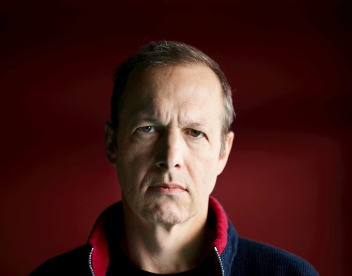 a man is staring straight ahead with a red background