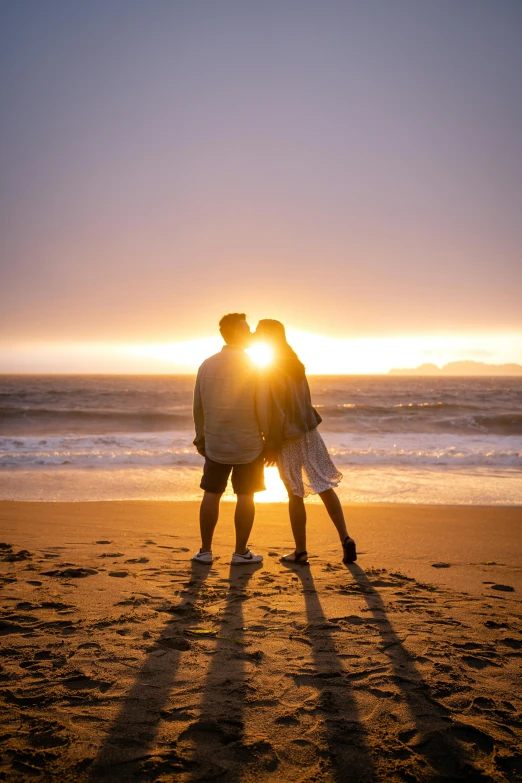 two people emcing while standing on a beach near the ocean