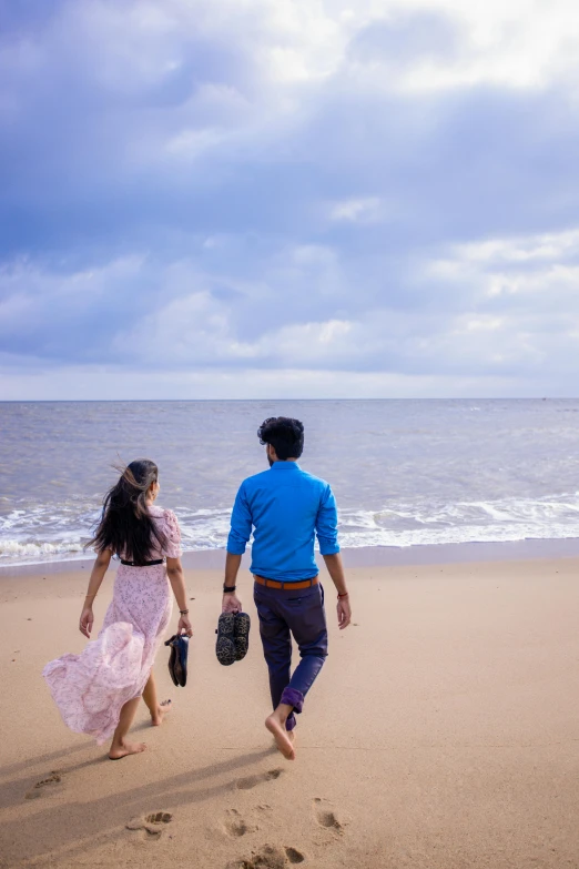 a young man and woman walking on a beach near the water