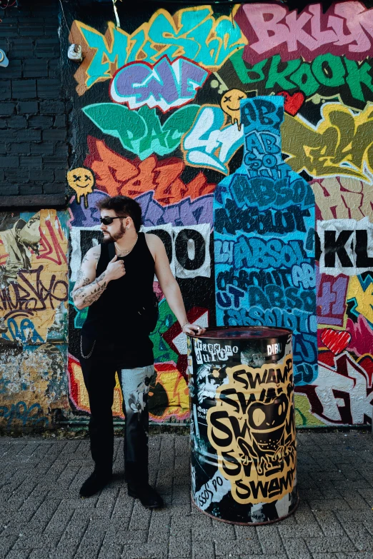 a man standing next to a trash can with graffiti on the wall