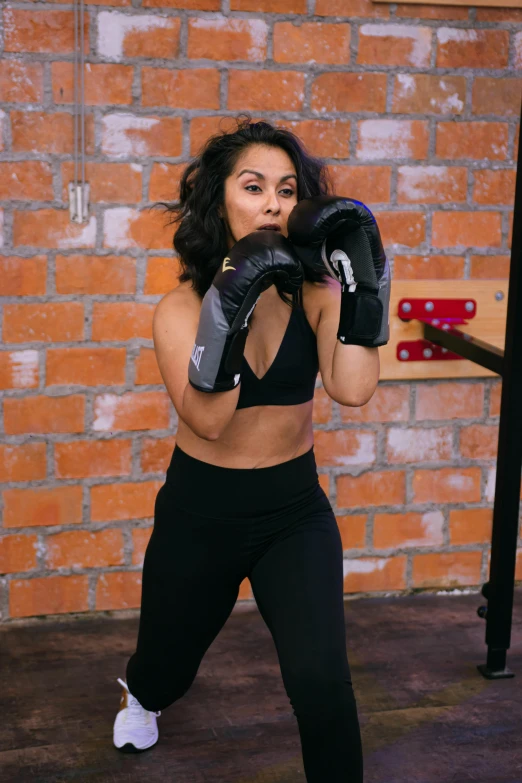 a girl standing in front of a brick wall holding a pair of boxing gloves