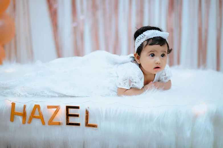 a baby wearing a white dress laying on top of a bed