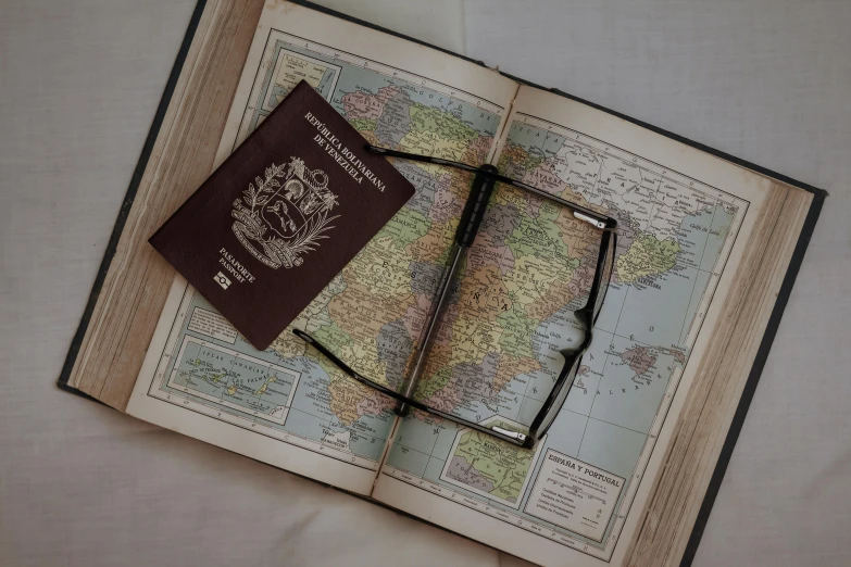 a passport, glasses, and a camera sit on top of an open book