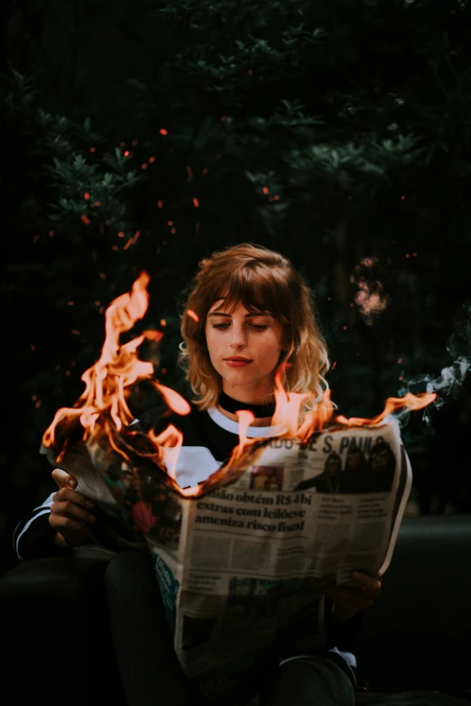 a woman is reading a newspaper surrounded by flames
