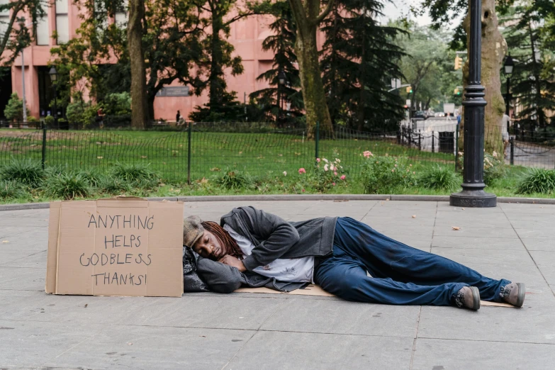 a man asleep on the ground in front of a brown sign with writing written on it