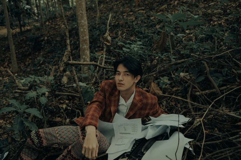 the young man is sitting in the woods holding a paper