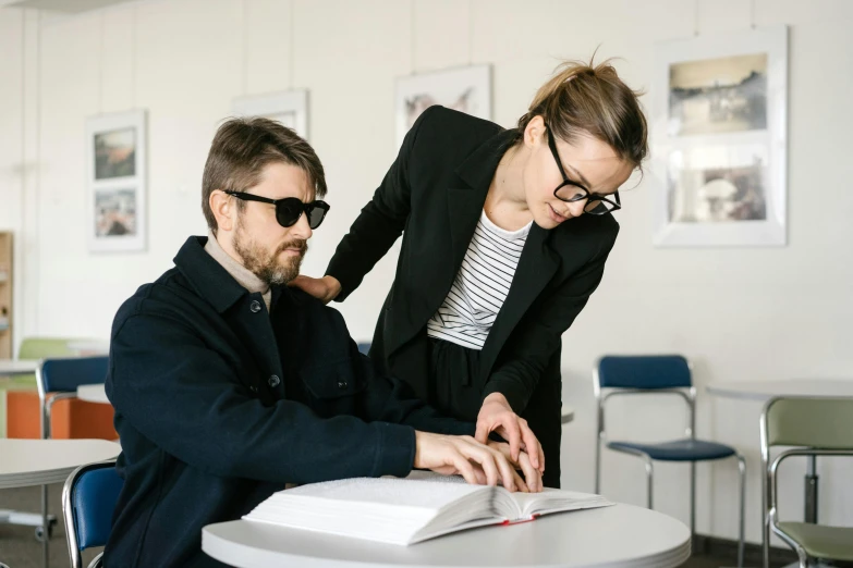 two people are standing and looking at an open book