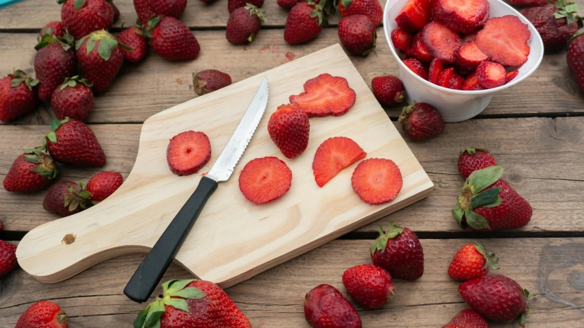 cut up strawberries sit on a  board next to a knife