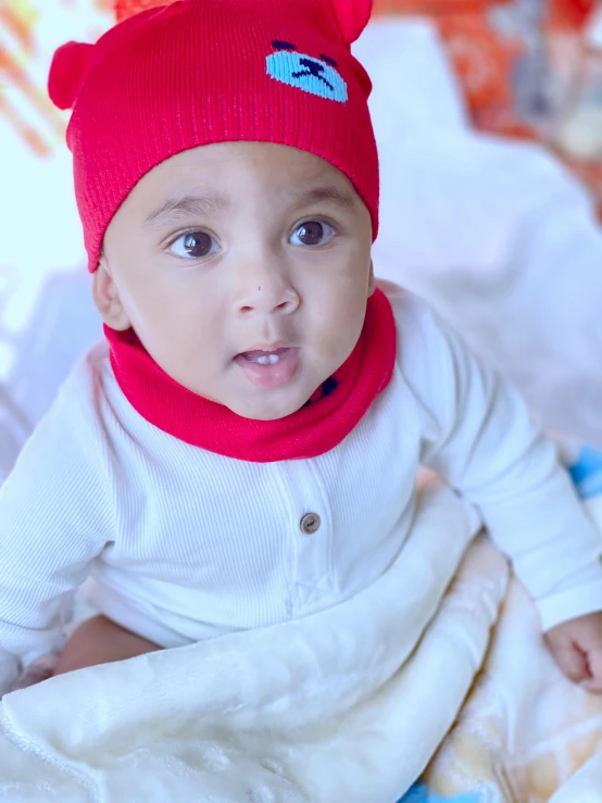 baby wearing a red bear hat and white outfit